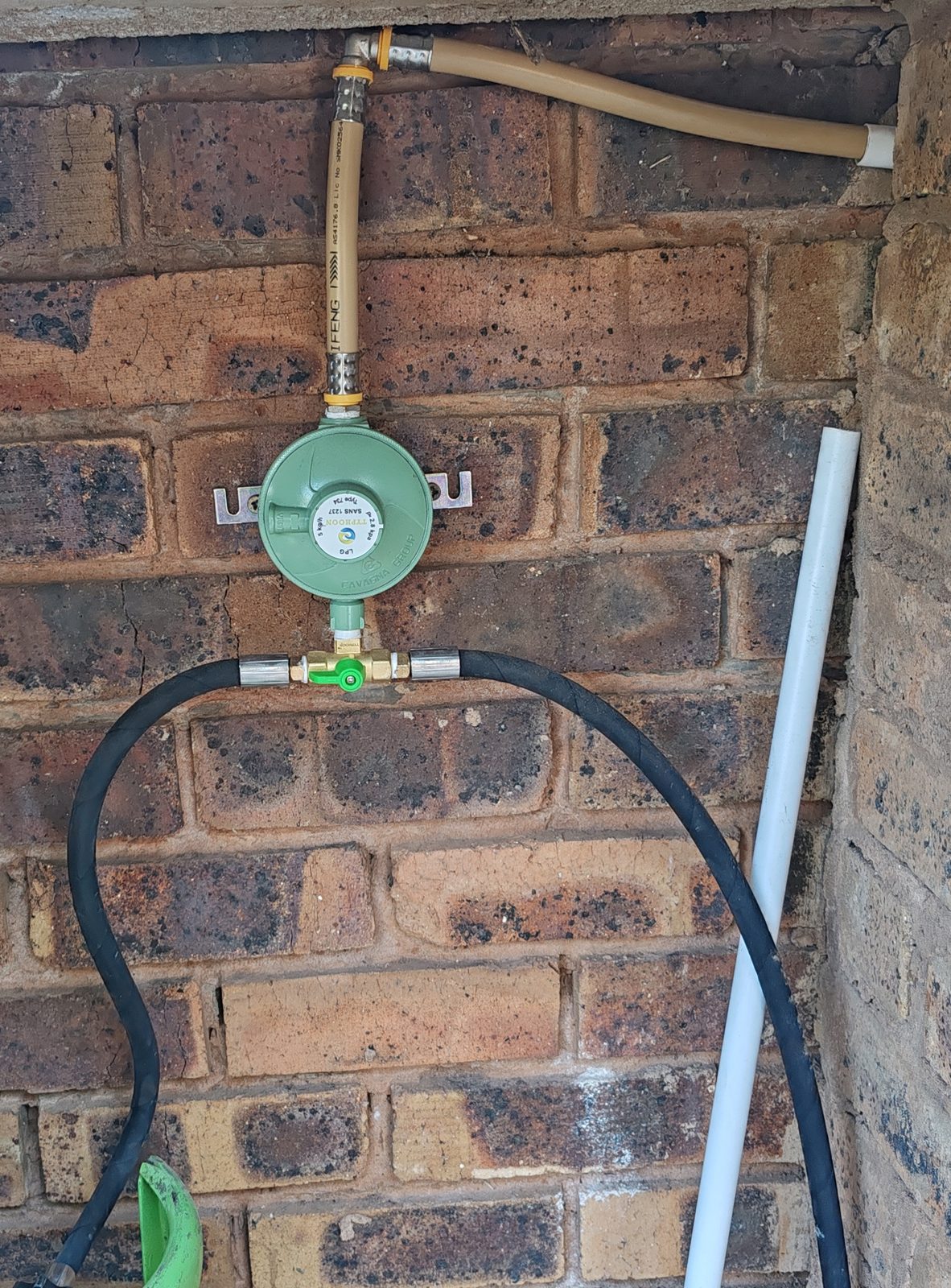 Close-up of gas regulator and pipe connection mounted on brick wall
