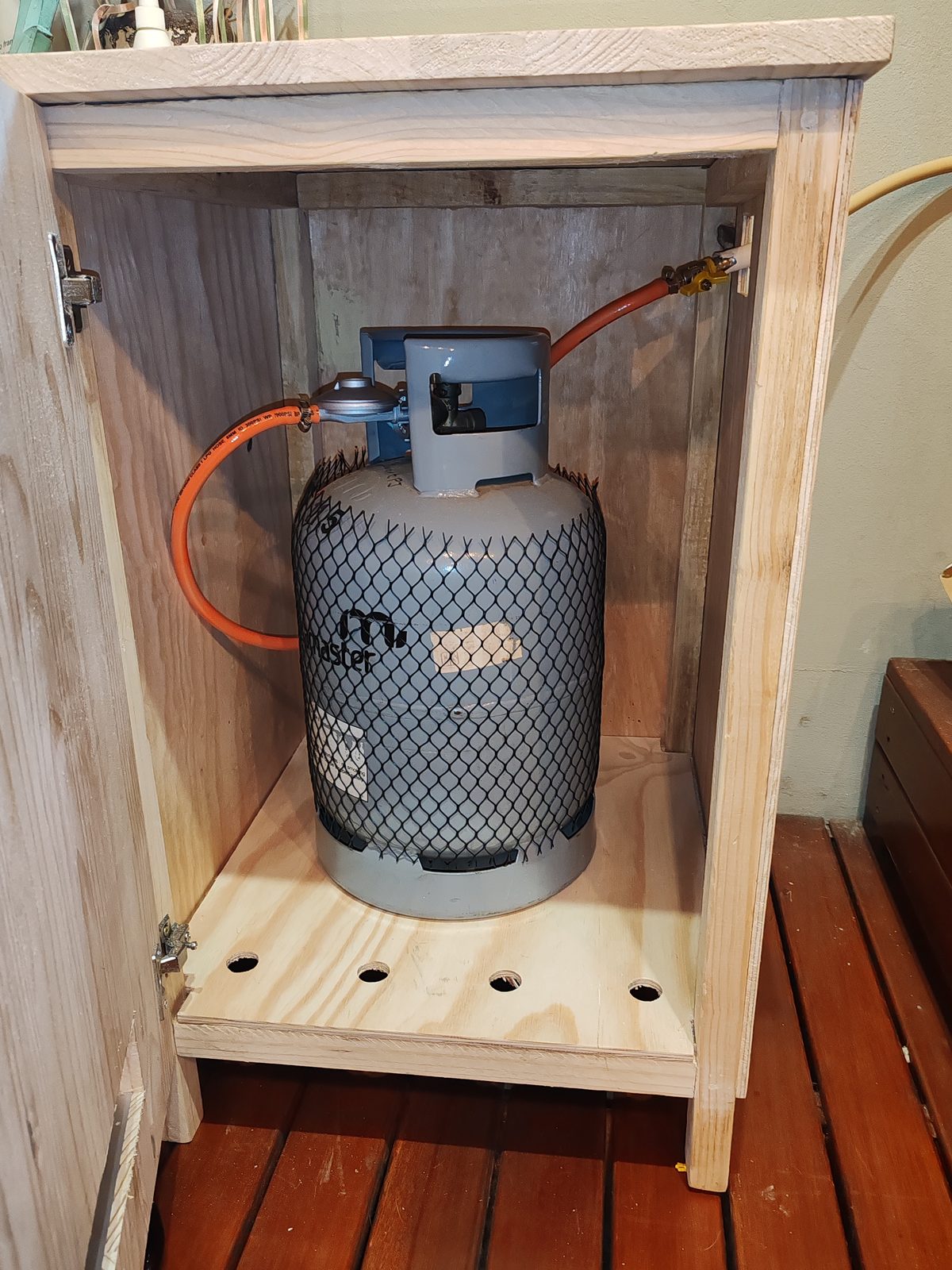 Gas cylinder inside custom wooden cabinet with orange hose connection