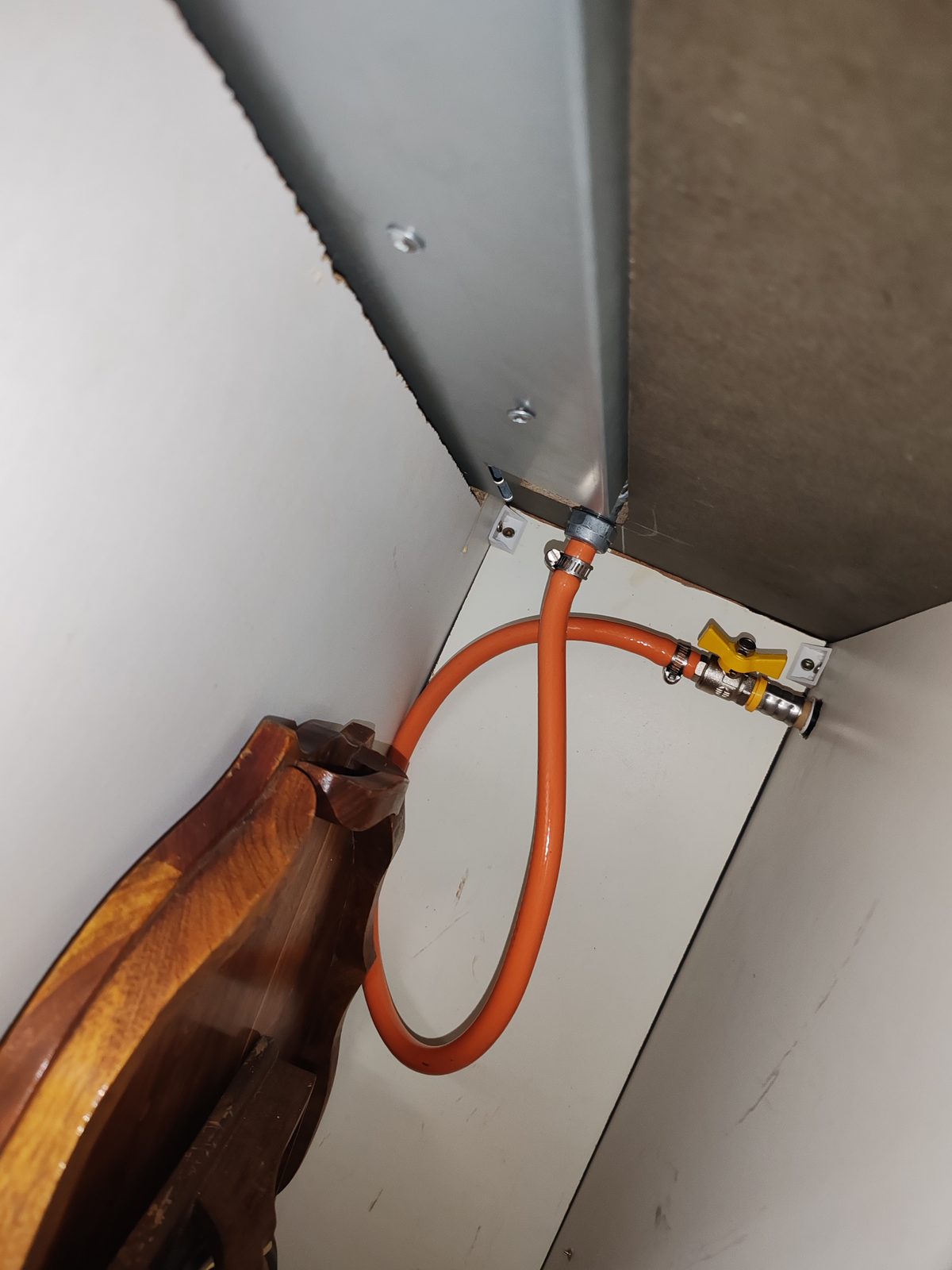 Orange gas hose and shut off valve connection behind appliance